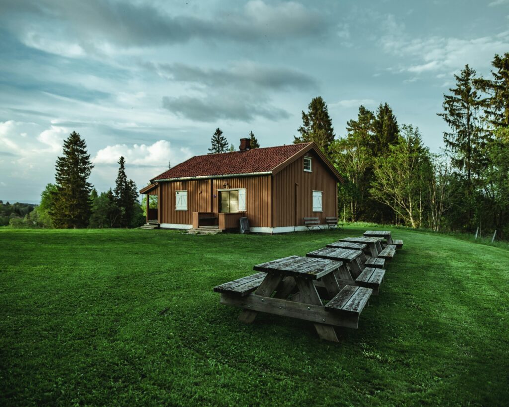 A rustic house in Norway's peaceful countryside, surrounded by lush greenery and wooden furniture.
